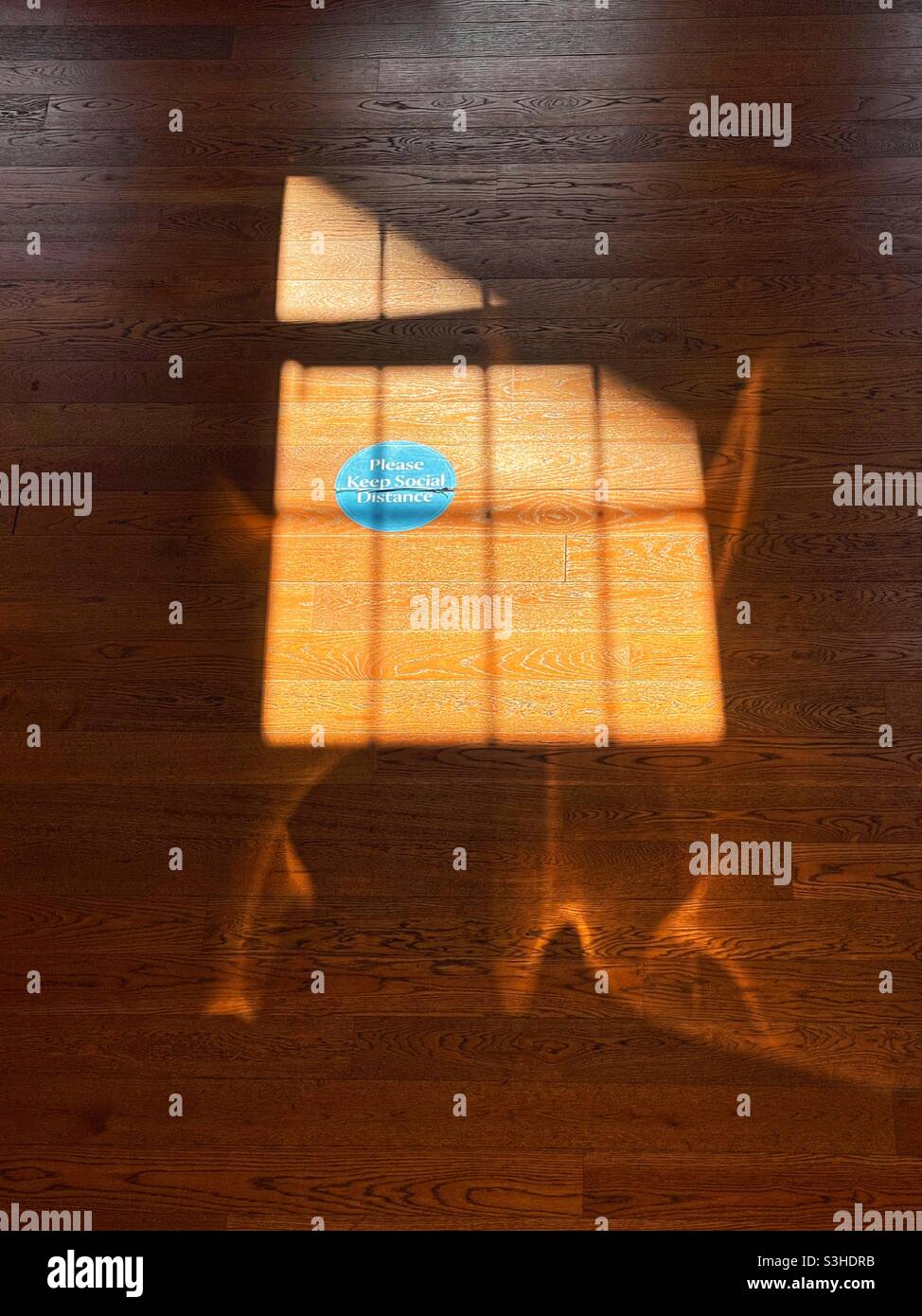 Social distancing sticker on a wooden floor lit by sunlight from a window frame Stock Photo
