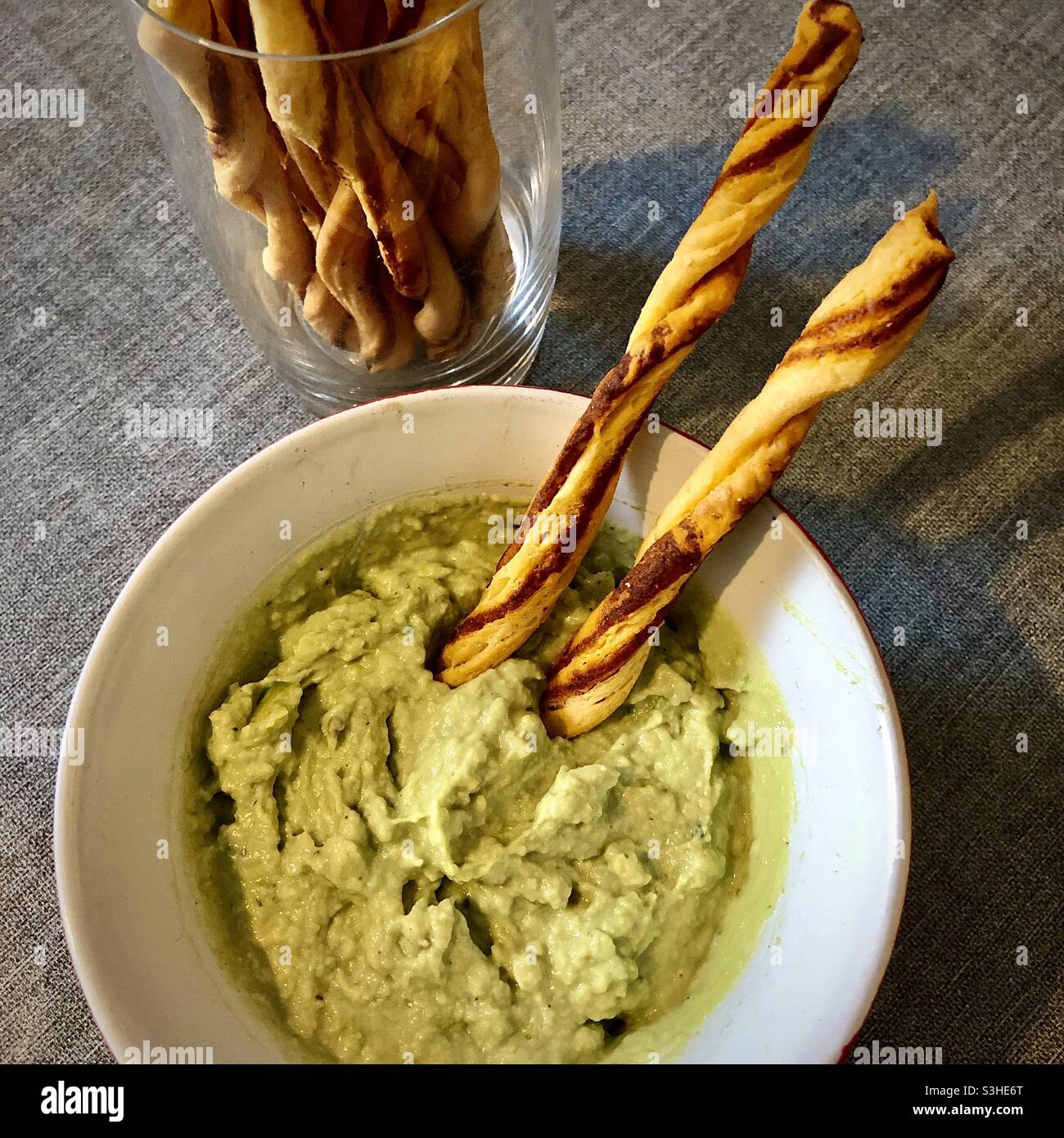 Homemade avocado dip in bowl with commercial breadsticks. Stock Photo