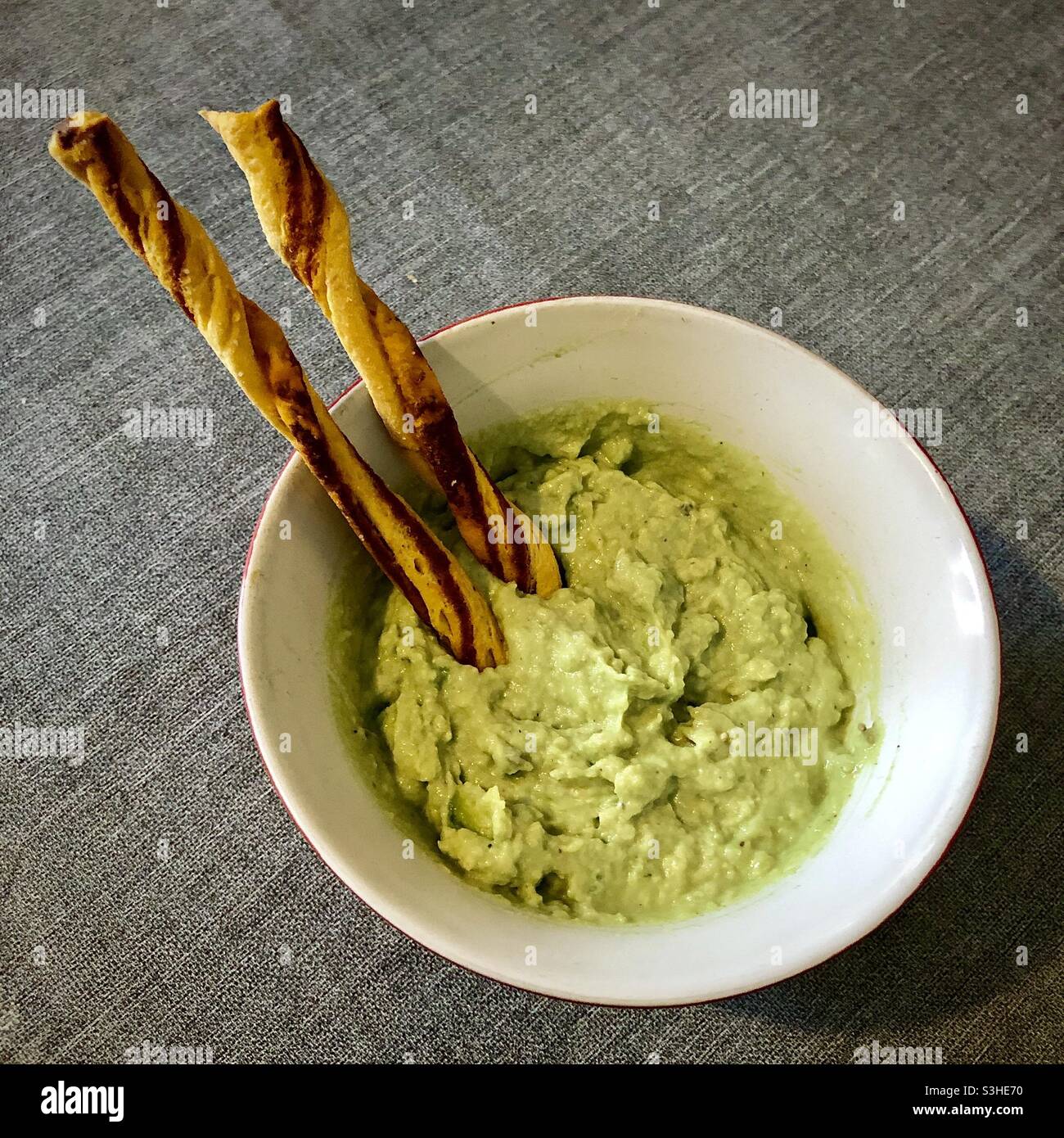 Homemade avocado dip in bowl with breadsticks. Stock Photo