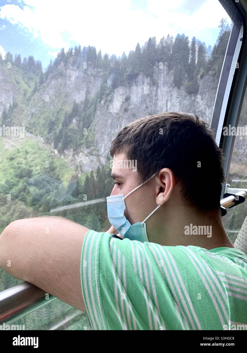 Tourist with a face mask in a cable car sdmiring landscpe in Switzerland. Stock Photo