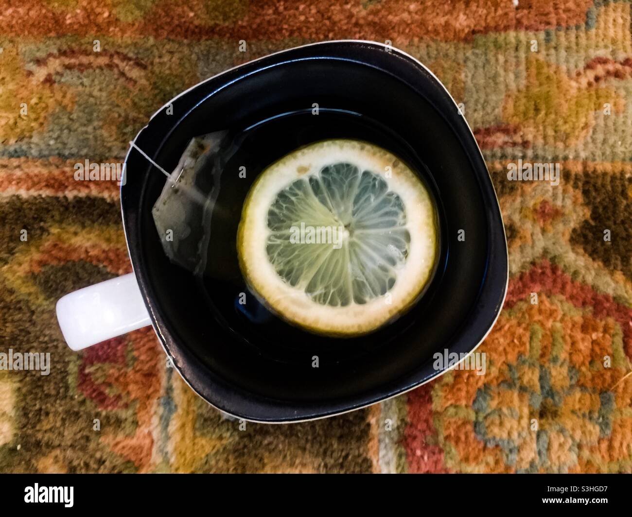 Green tea with slice of fresh lemon, a healthful drink, sitting on an oriental rug, Canada. Often combined with honey, ginger, and herbs. Stimulating infusion. Asian. - Smartphone Captured Stock Image