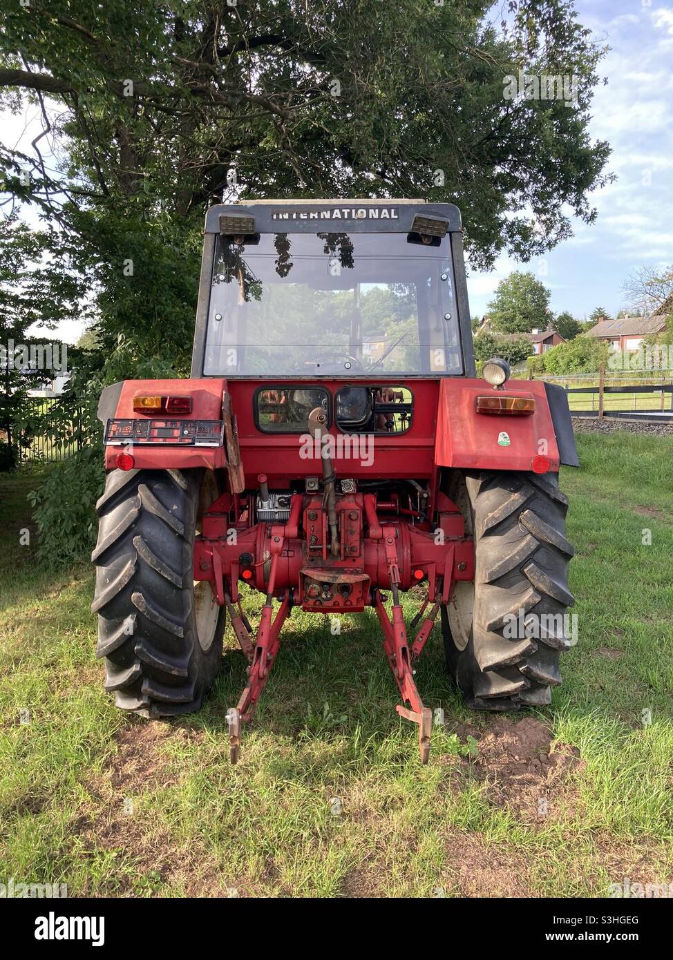 a red tractor that can be seen from behind stands on a meadow in front of a tree - Smartphone Captured Stock Image