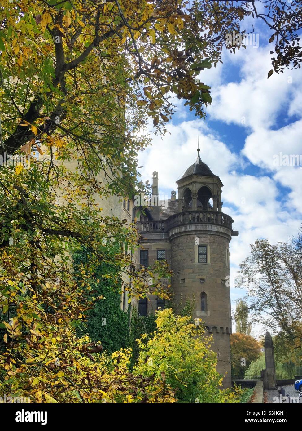 Tower of the water castle in Neuenstein in Germany framed by branches with autumnal colored leaves - Smartphone Captured Stock Image