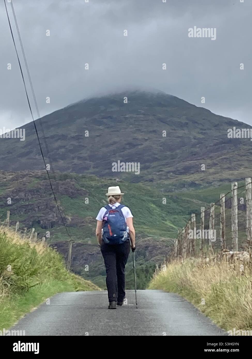 A female Walker on a small country road with a mountain in the background in Snowdonia - Smartphone Captured Stock Image