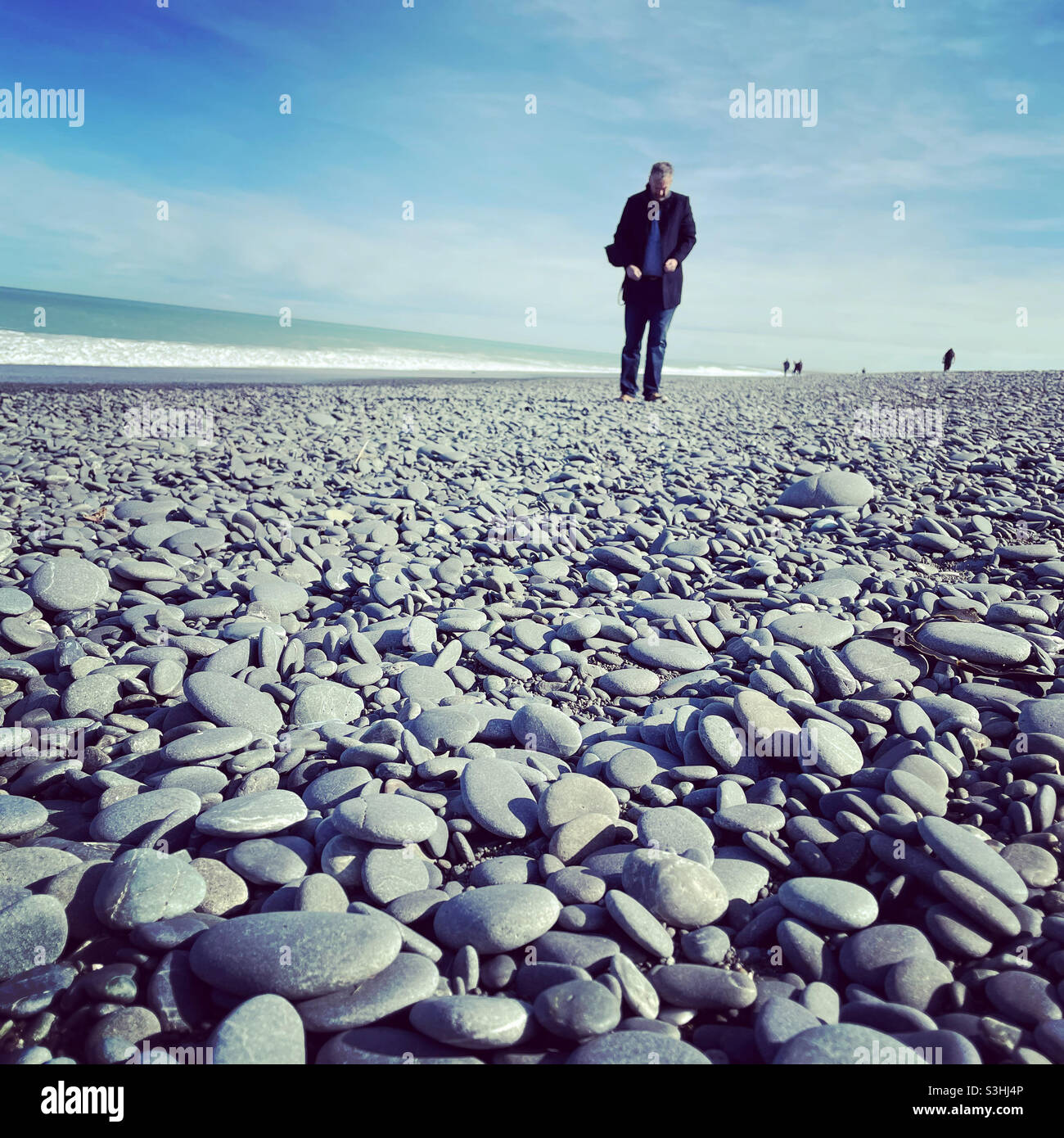 A man walks alone on a rocky beach at Birdlings Flat in New Zealand - Smartphone Captured Stock Image