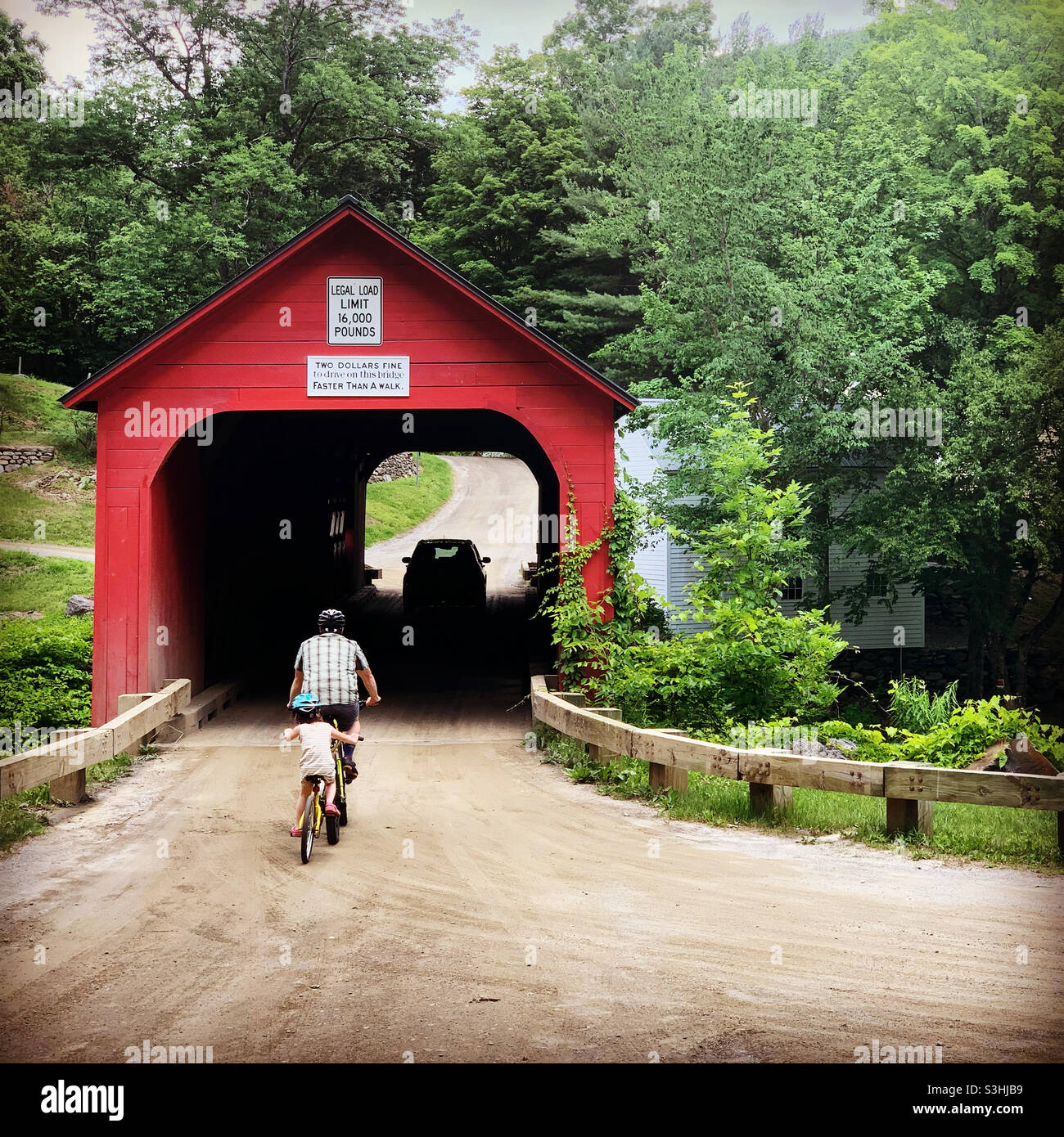 June, 2021, an adult and child crossing the Green River Covered Bridge on bicycles, Guilford, Windham County, Vermont, United States - Smartphone Captured Stock Image