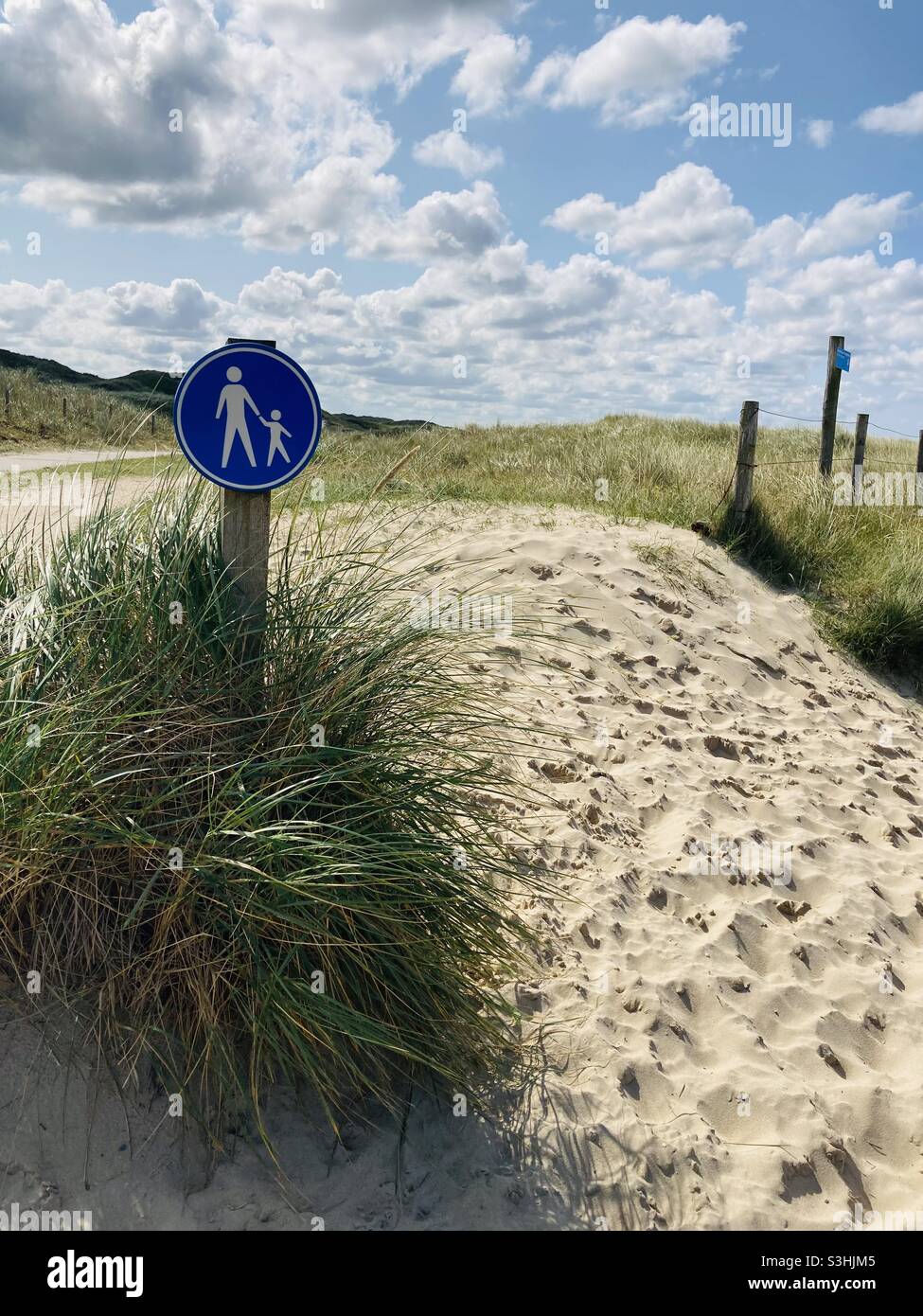 a blue pedestrian sign stands in the dunes on a beautiful summer's day and indicates a sandy path overgrown with dune grass Stock Photo