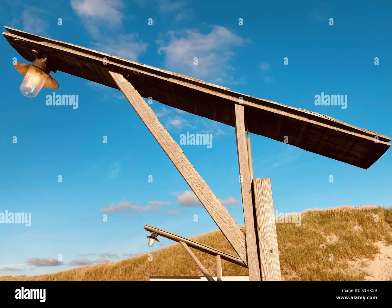a burning lamp against a blue sky in broad daylight attached to a wooden gallows Stock Photo