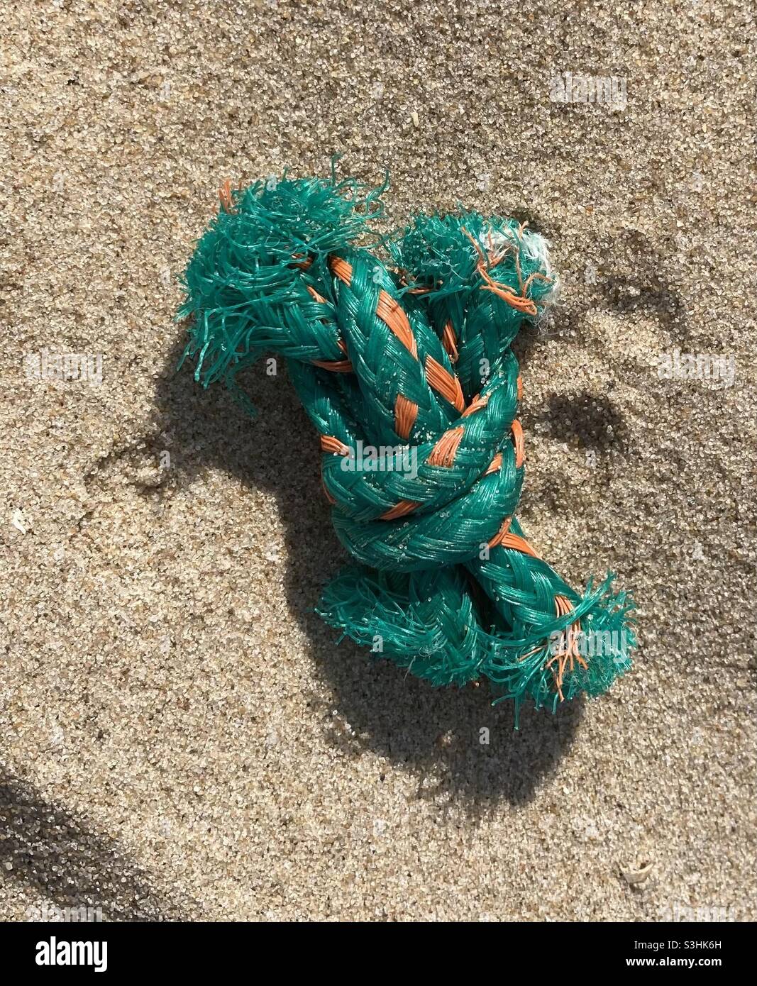 in the sand on the beach there is a green-orange knotted piece of a fishing net in the sun - Smartphone Captured Stock Image