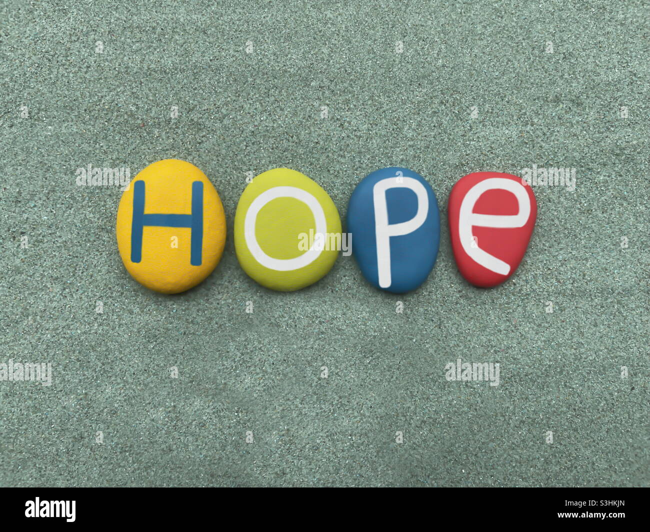 Hope, creative text composed with multi colored stone letters over green sand - Smartphone Captured Stock Image