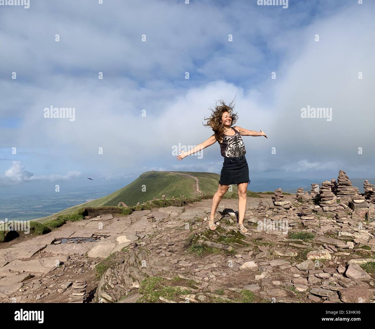 Woman with arms open at top of corn du with pen y fan in the background Stock Photo