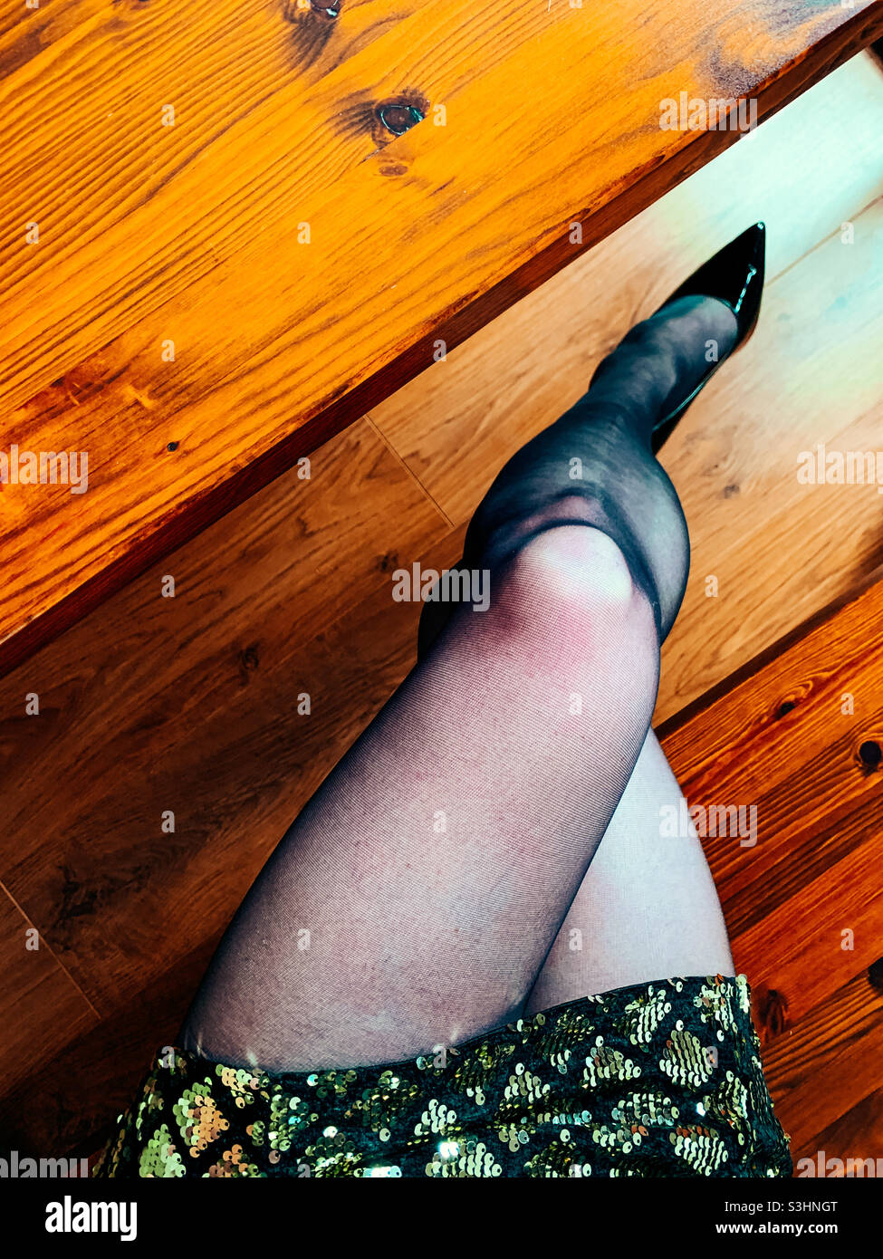 Crossed legged woman wearing a sequin dress sat at a table - Smartphone Captured Stock Image