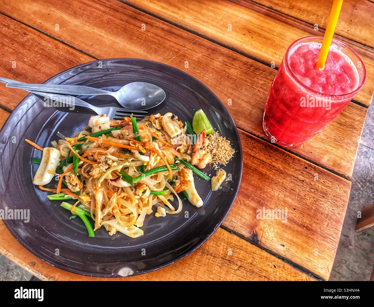Pad Thai noodles and a watermelon shake on a wooden table on the island of Koh Lipe in Thailand - Smartphone Captured Stock Image