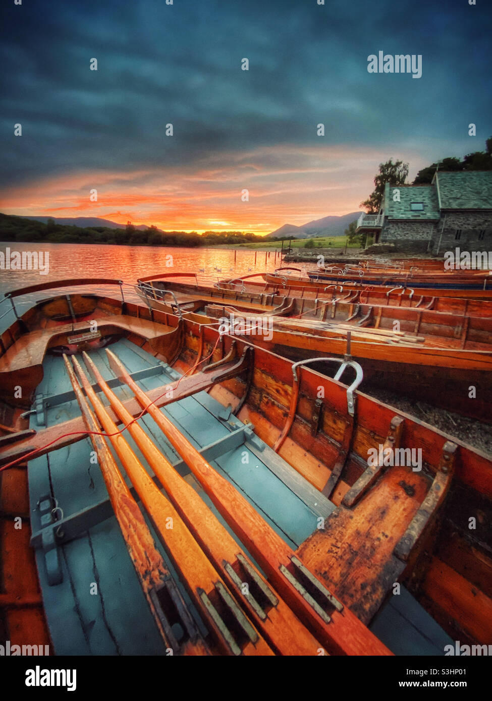 Rowing boats pulled up on beach by Derwent Water at Keswick as the sun sets Stock Photo