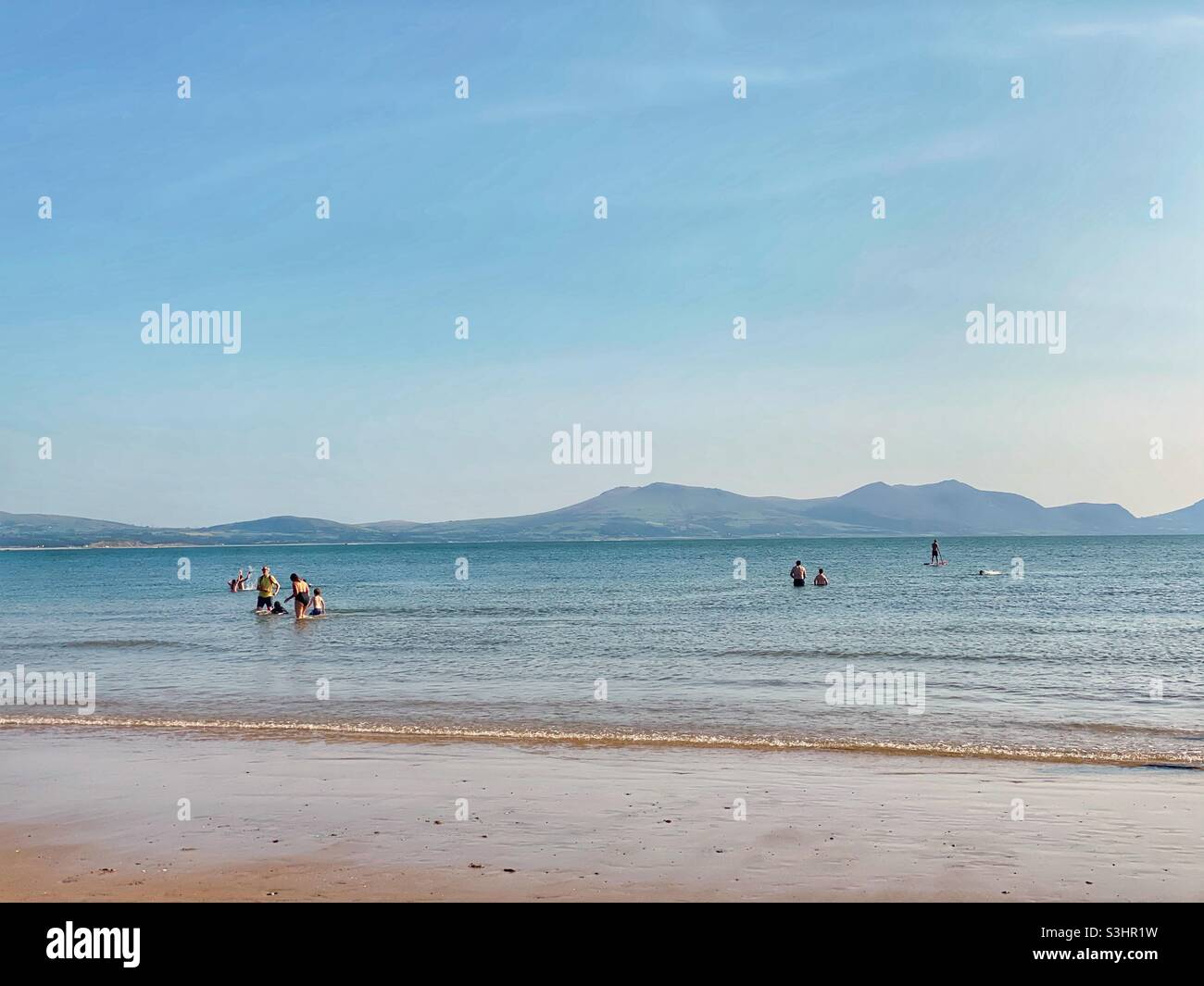 People swimming in the sea at Newborough beach with the Snowdonia mountain range in the distance, Anglesey, North Wales, UK, late summer 2021, August - Smartphone Captured Stock Image