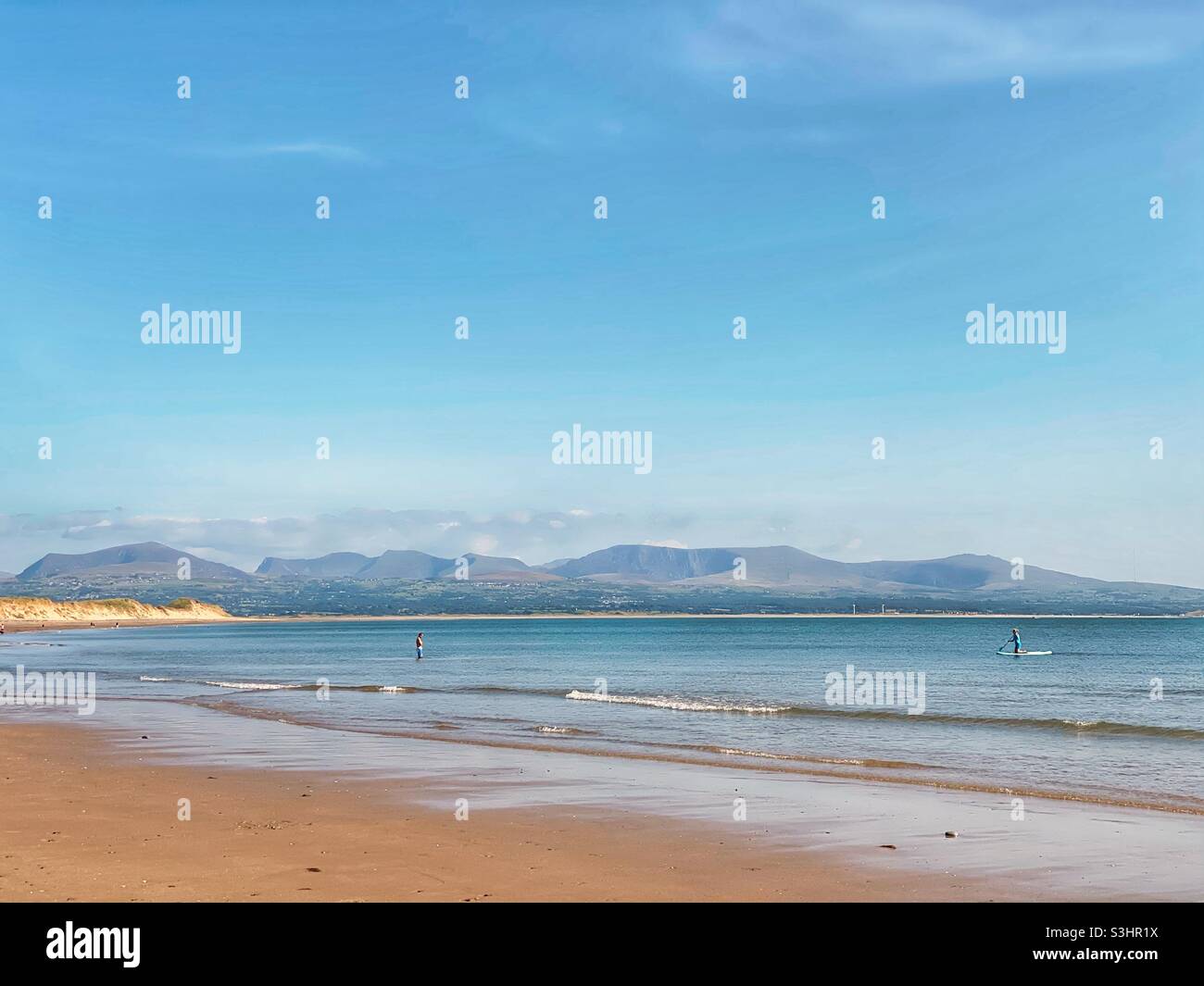 Bathing and paddle boarding off the coast of Anglesey on Newborough beach with the Snowdonia mountain range in the background, uk, late summer, 2021 - Smartphone Captured Stock Image