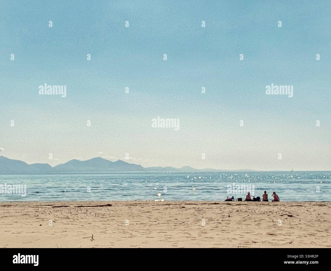 Group of people gathered on quiet part of Newborough beach by Newborough Warren, hot late august summer day, Snowdonia mountain range in background - Smartphone Captured Stock Image