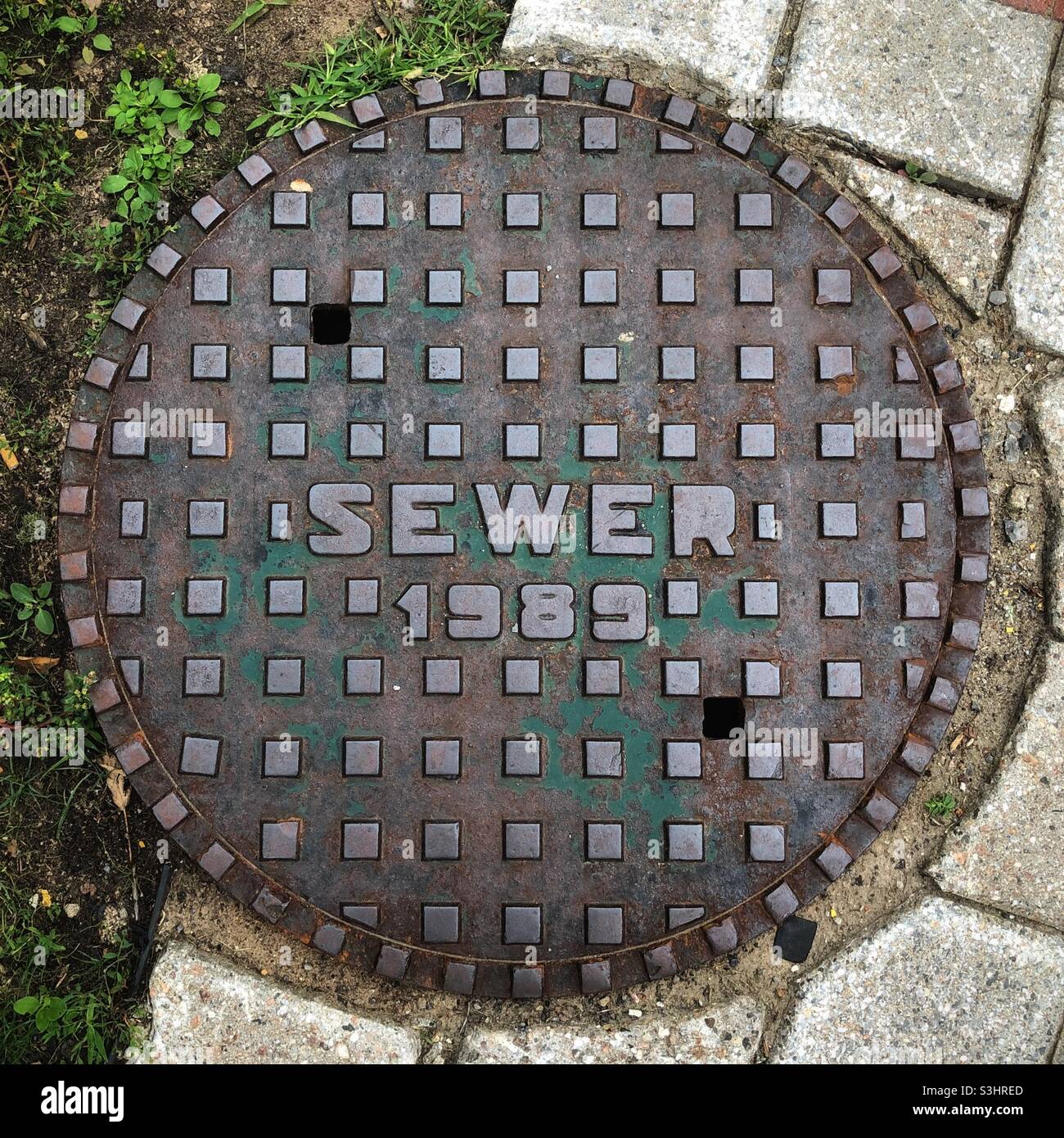 Manhole cover reading SEWER 1989 in part on sidewalk, in part on the