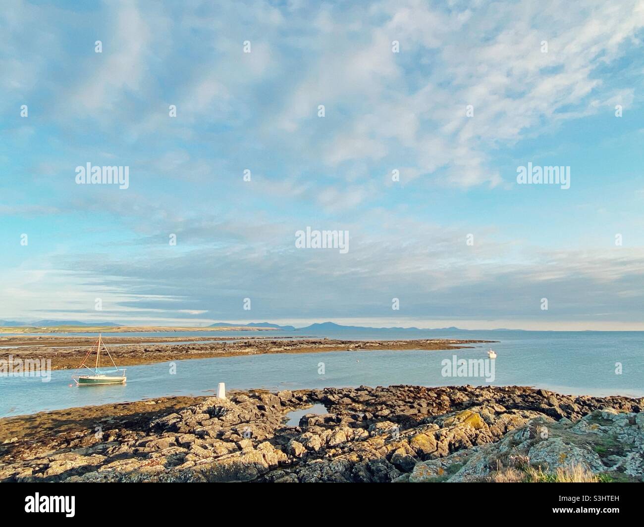 Sail boat moored in boat pool at Rhosneigr beach, Anglesey, North Wales, UK, Snowdonia mountain range in background, late summer, at sunset - Smartphone Captured Stock Image