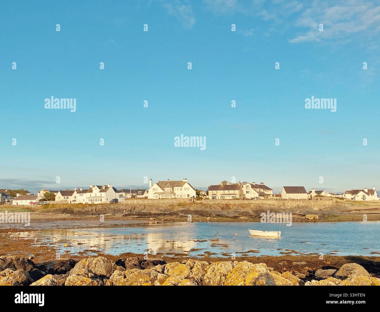 Rhosneigr beach early evening in late August as the sun sets over the houses, looking back at the village from the beach across the boat pool, Anglesey, North Wales, UK Stock Photo