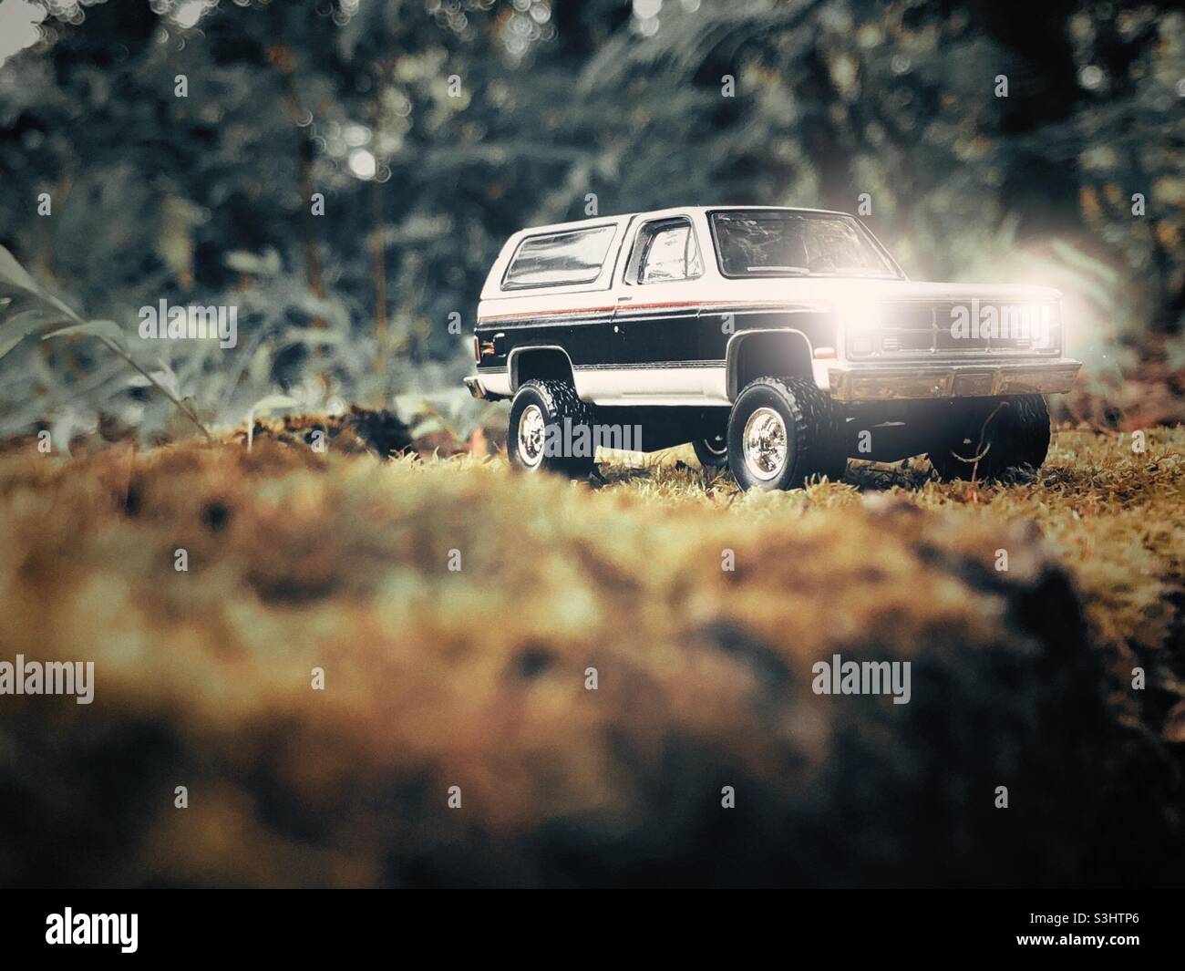 Small toy 4x4 SUV on a moss covered cinder block. Headlight illumination added in post processing. Stock Photo