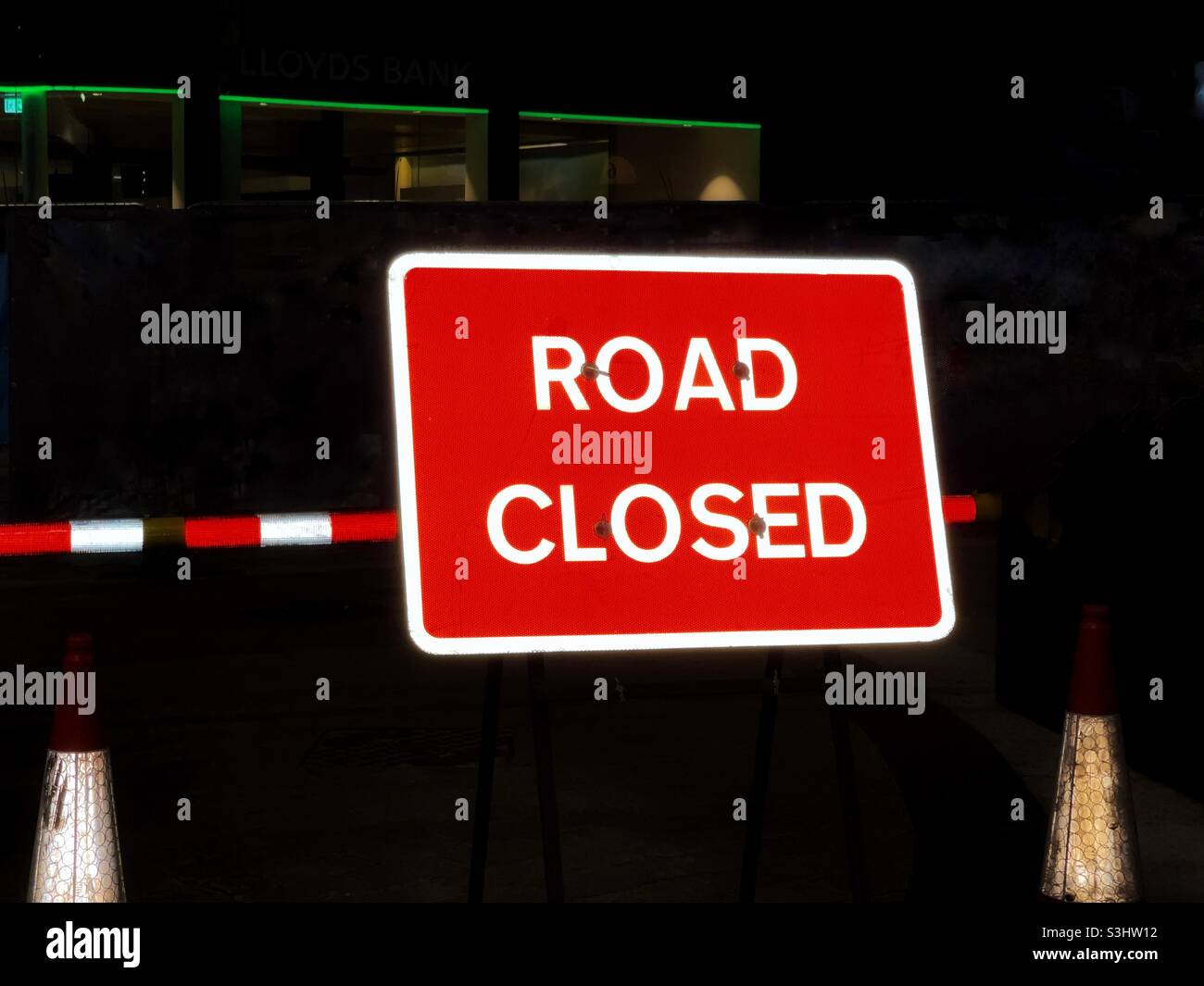 Road closed sign at night reflecting light from car headlights Stock Photo