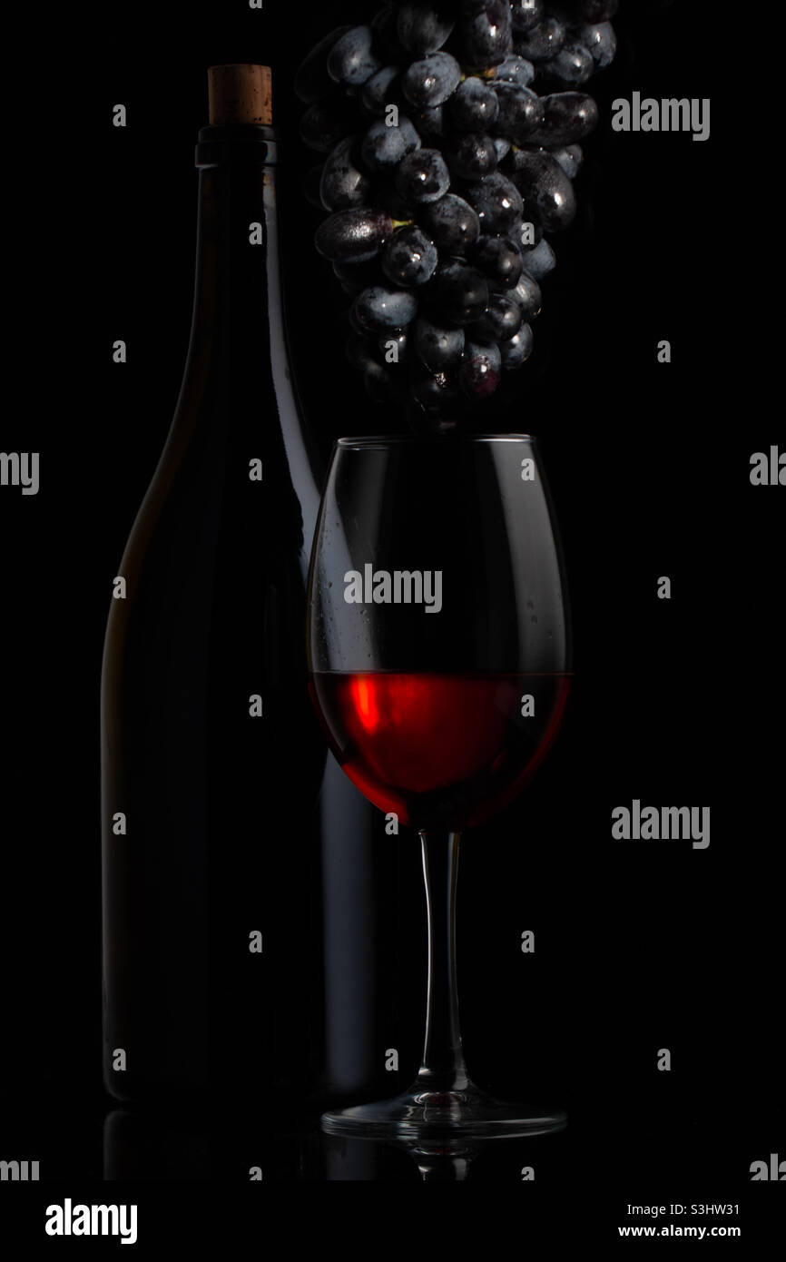 Red wine, a bottle and a glass with ripe grapes, a still life on a ...