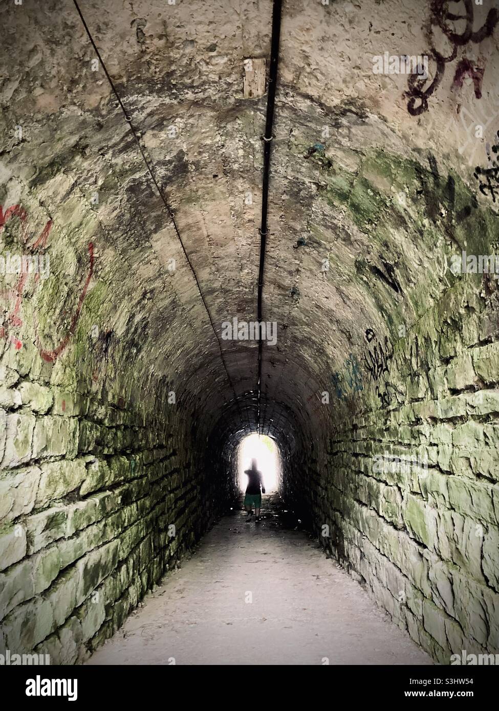 Anonymous silhouette walking through a dark under pass simbolizing light at the end of the tunnel Stock Photo