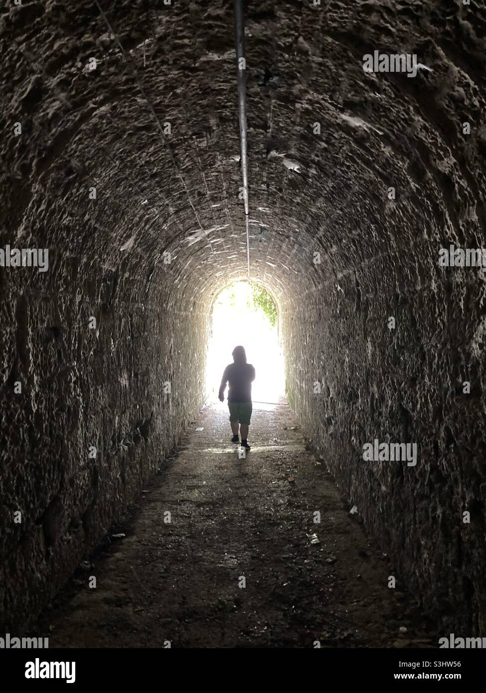 Anonymous silhouette of a man walking through a dark underpass symbolizing light at the end of a tunnel Stock Photo