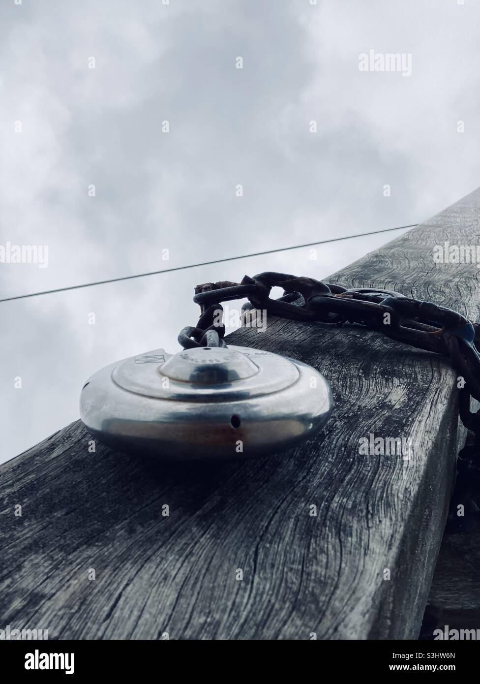 a round padlock hangs on a wooden beam around which a metal chain is wrapped - Smartphone Captured Stock Image