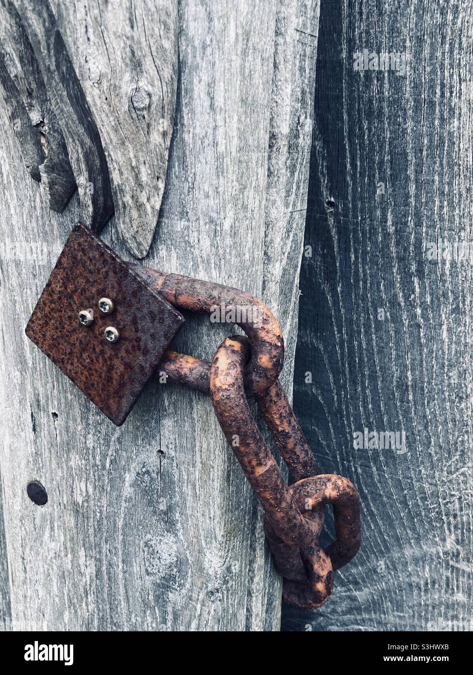 A rusty chain is attached to a gray wooden post - Smartphone Captured Stock Image