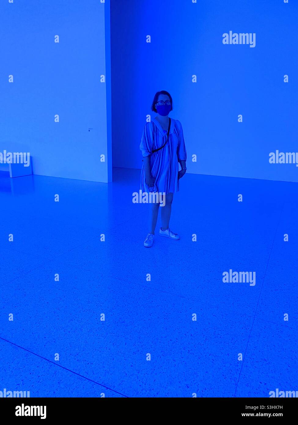 Masked museum visitor bathed in blue light at the Walker Art Center. Stock Photo
