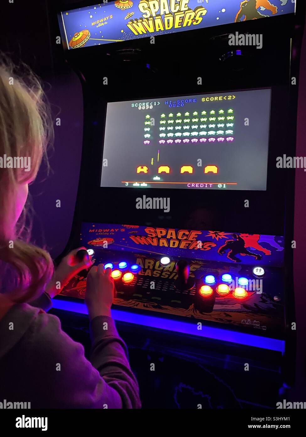 Teenager playing on a retro arcade space invaders Machine - Smartphone Captured Stock Image