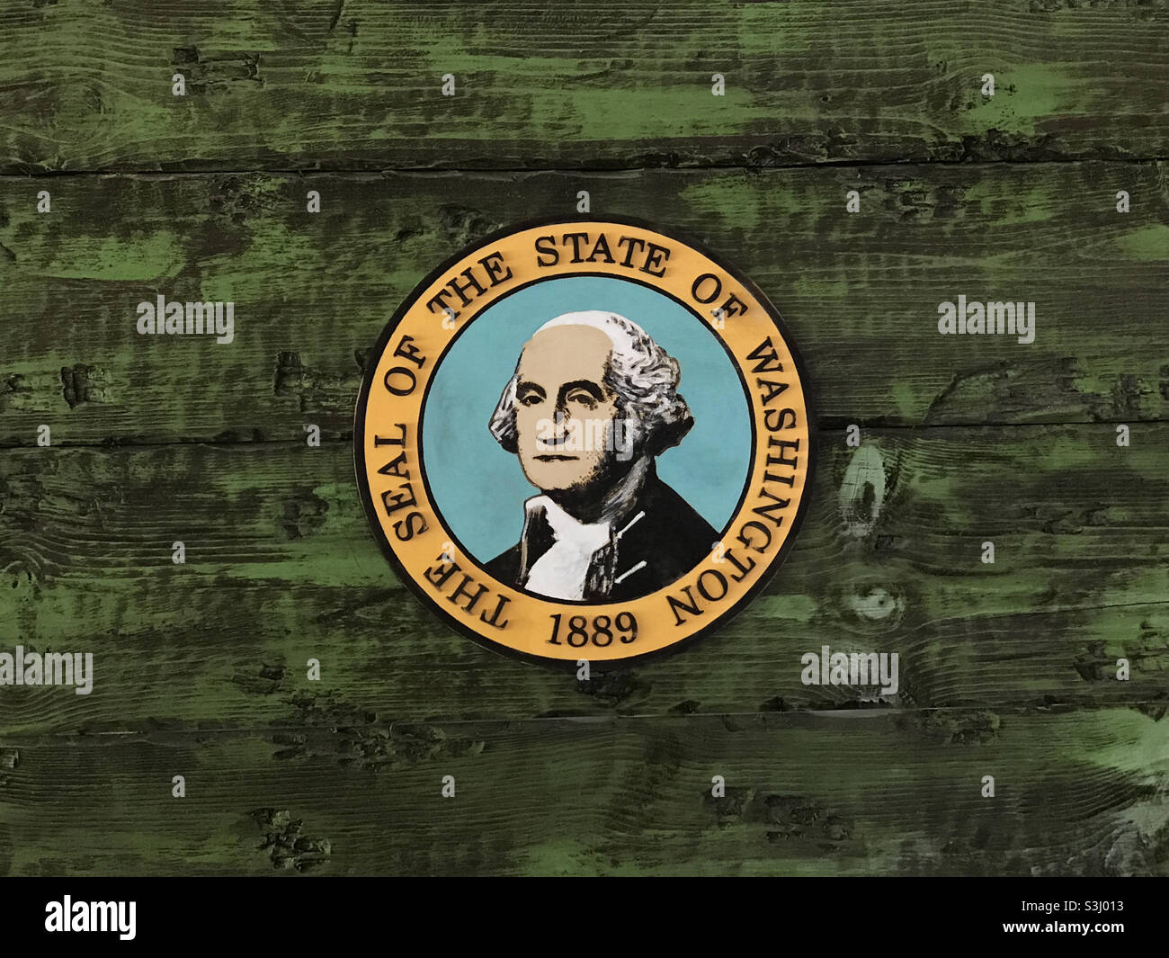 The state seal of Washington, USA, featuring George Washington in the center, is shown mounted on a rustic wall painted green. - Smartphone Captured Stock Image