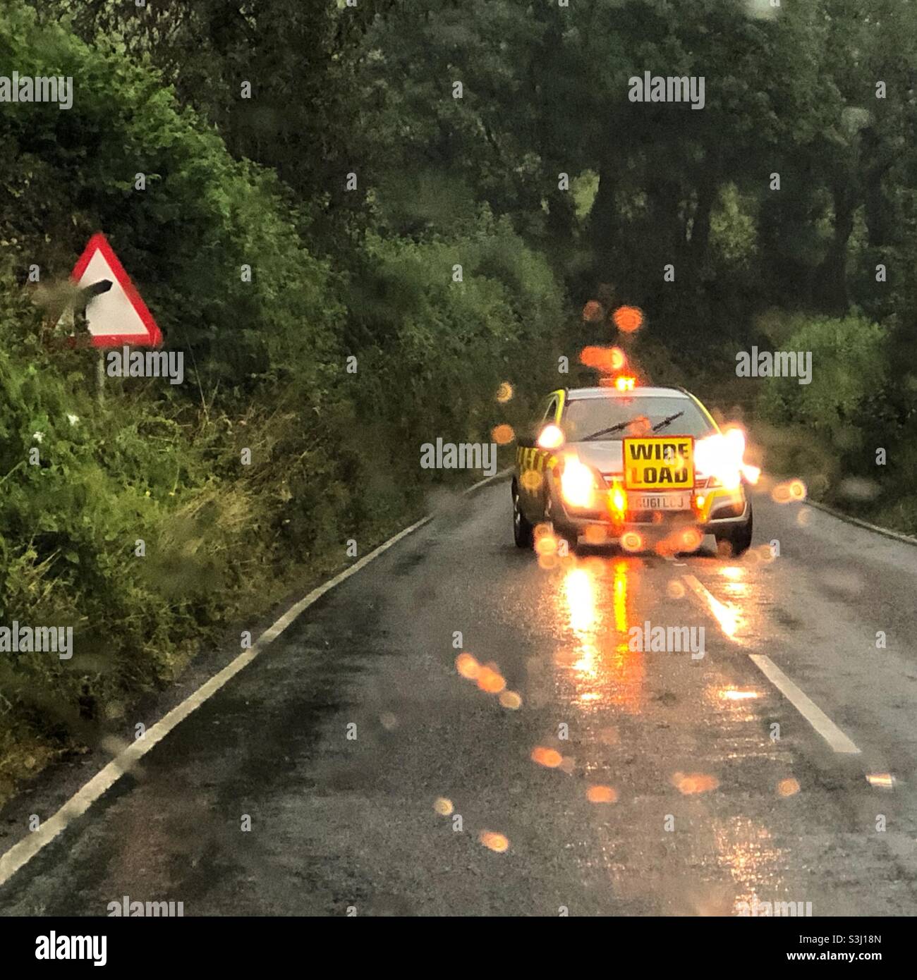Wide load support vehicle blocks a road to oncoming traffic in wet driving conditions. Stock Photo