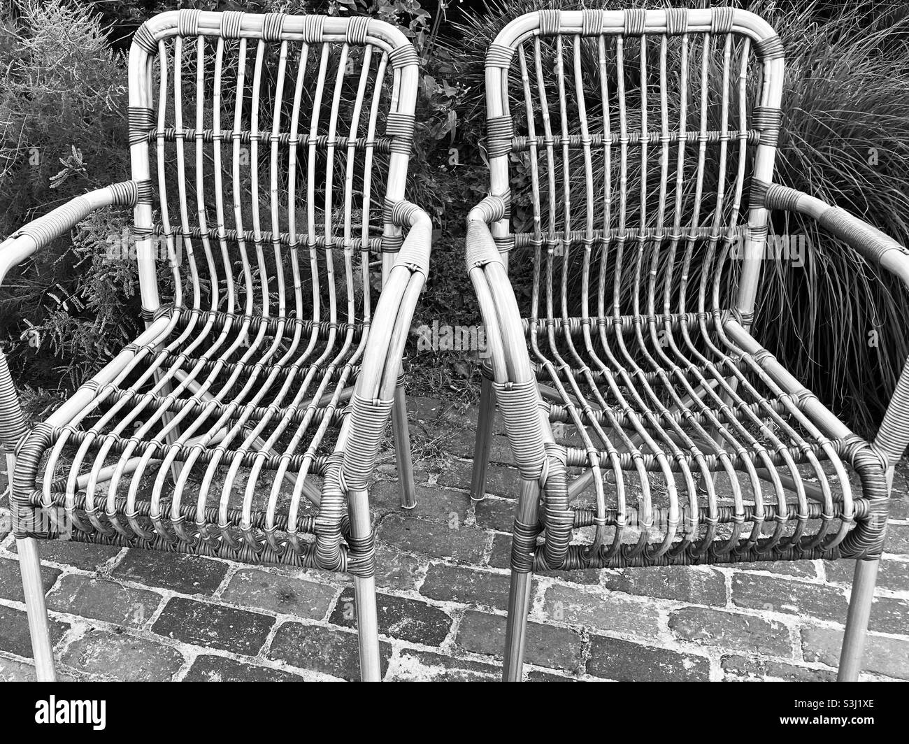 Two empty wicker chairs stand side by side in the garden Stock Photo