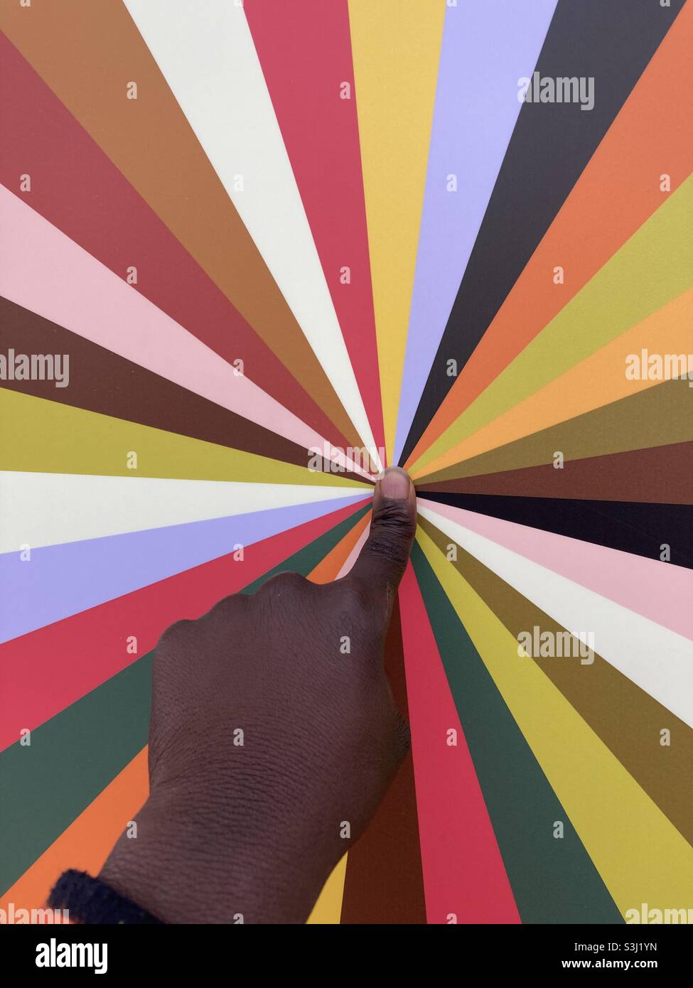 An index finger points to the center of a panel with color rays - Smartphone Captured Stock Image