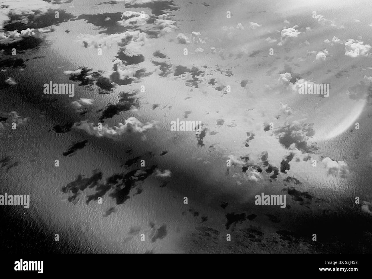 Floating clouds and reflections over the ocean in monochrome, from 30000 feet. Somber B&W. Silver, dark tones, and flair in the sky. - Smartphone Captured Stock Image