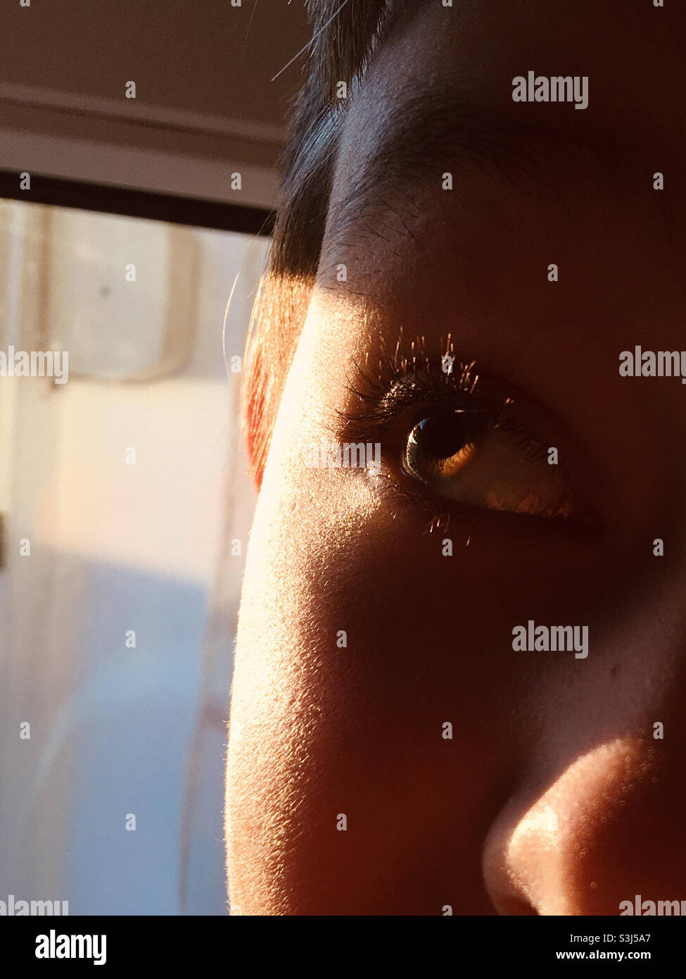 Boy child looking away, one eye, face illuminated by setting sun - Smartphone Captured Stock Image