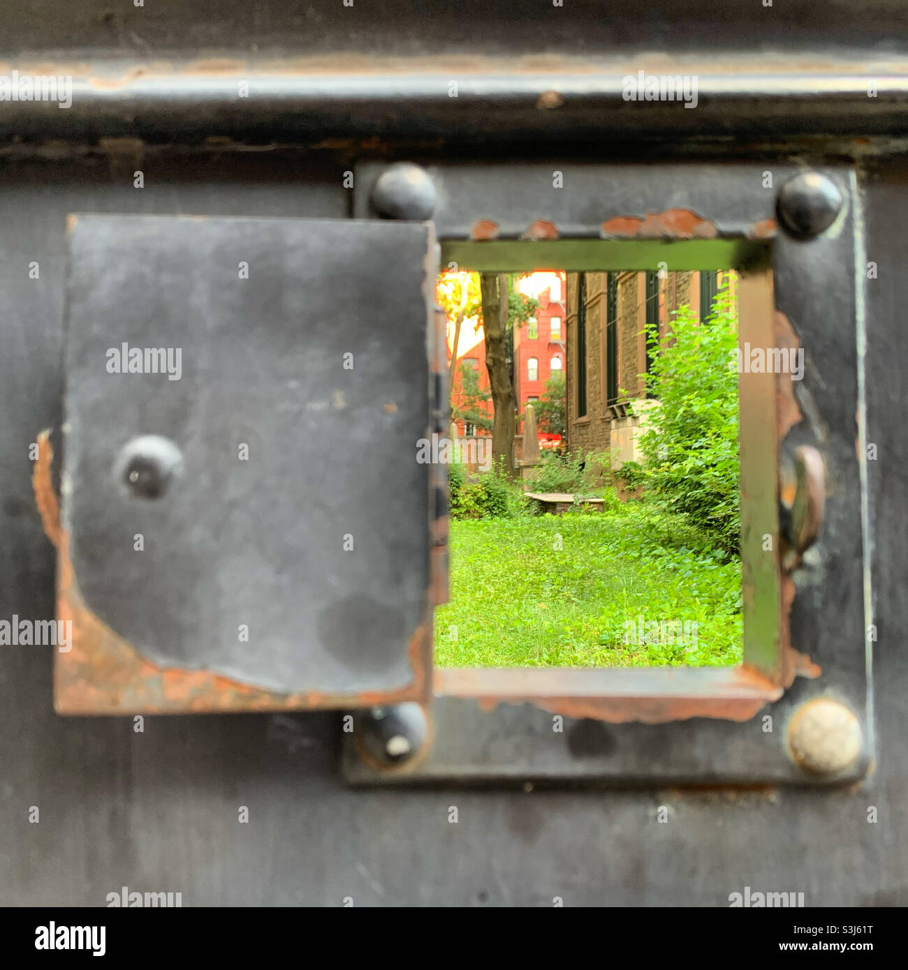 Looking through a window in the wall on the sidewalk towards the cemetery at Saint Michael’s Russian Catholic Church, NoLita, Manhattan, New York, New York, United States - Smartphone Captured Stock Image