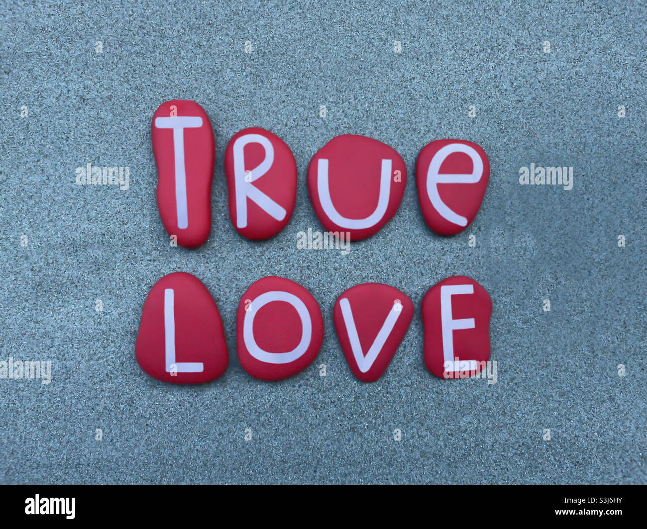 True love, creative message composed with red hand painted stone letters over green sand Stock Photo