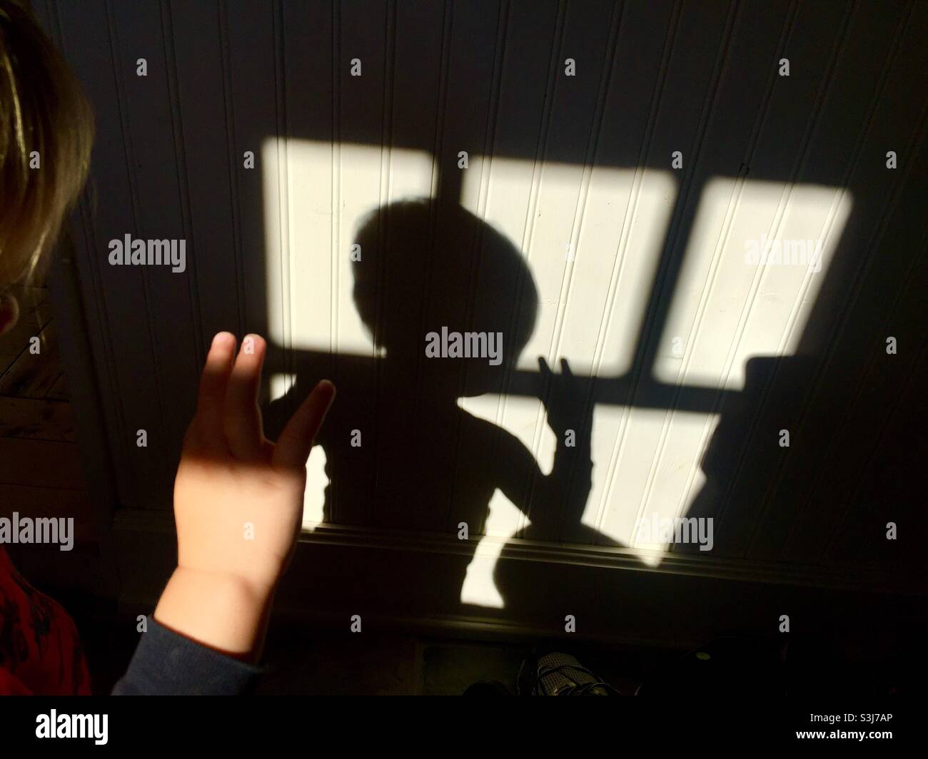 Child waving to his own shadow in the window. Toddler’s innocent play. Real moment. Hi! Hello! Bye bye. Goodbye. - Smartphone Captured Stock Image