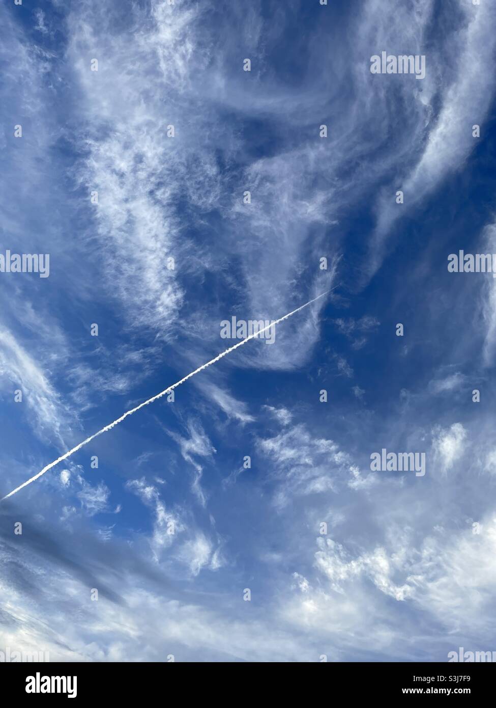 Deep blue skies with white fluffy clouds and airplane contrail - Smartphone Captured Stock Image