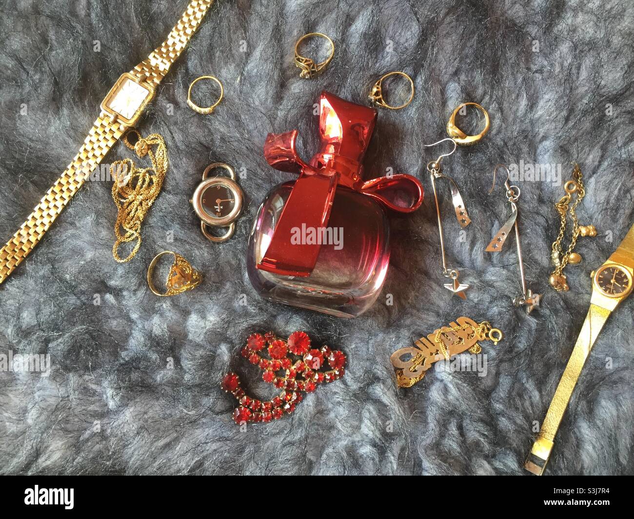 Red perfume with some golden rings and watches Stock Photo