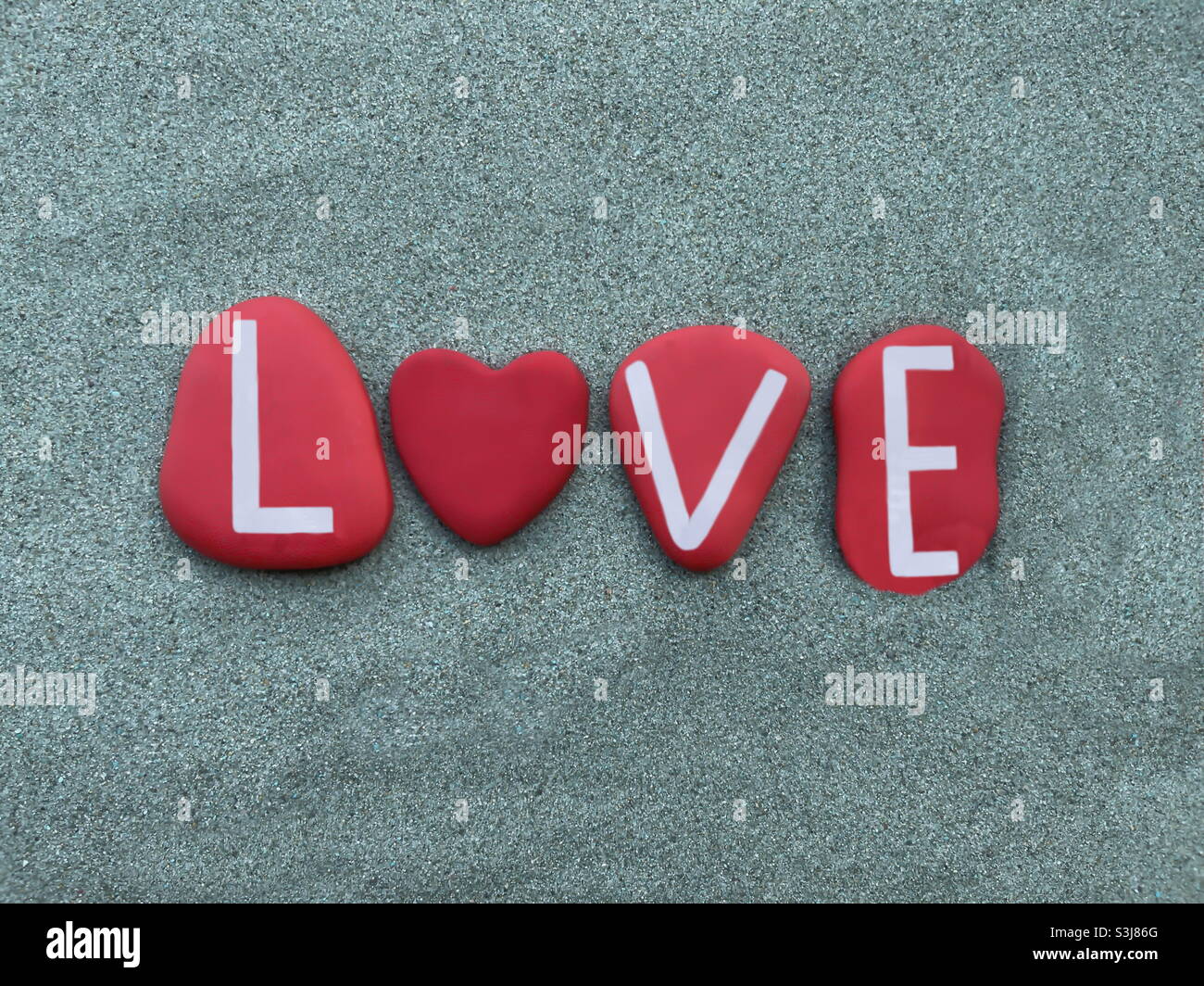 Love word composed with red colored stone letters and a red heart stone over green sand Stock Photo