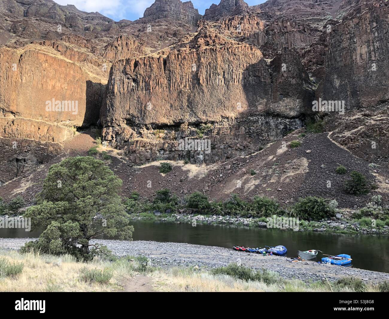 Boats on the shore below large cliffs on the John Day River in central Oregon. Stock Photo