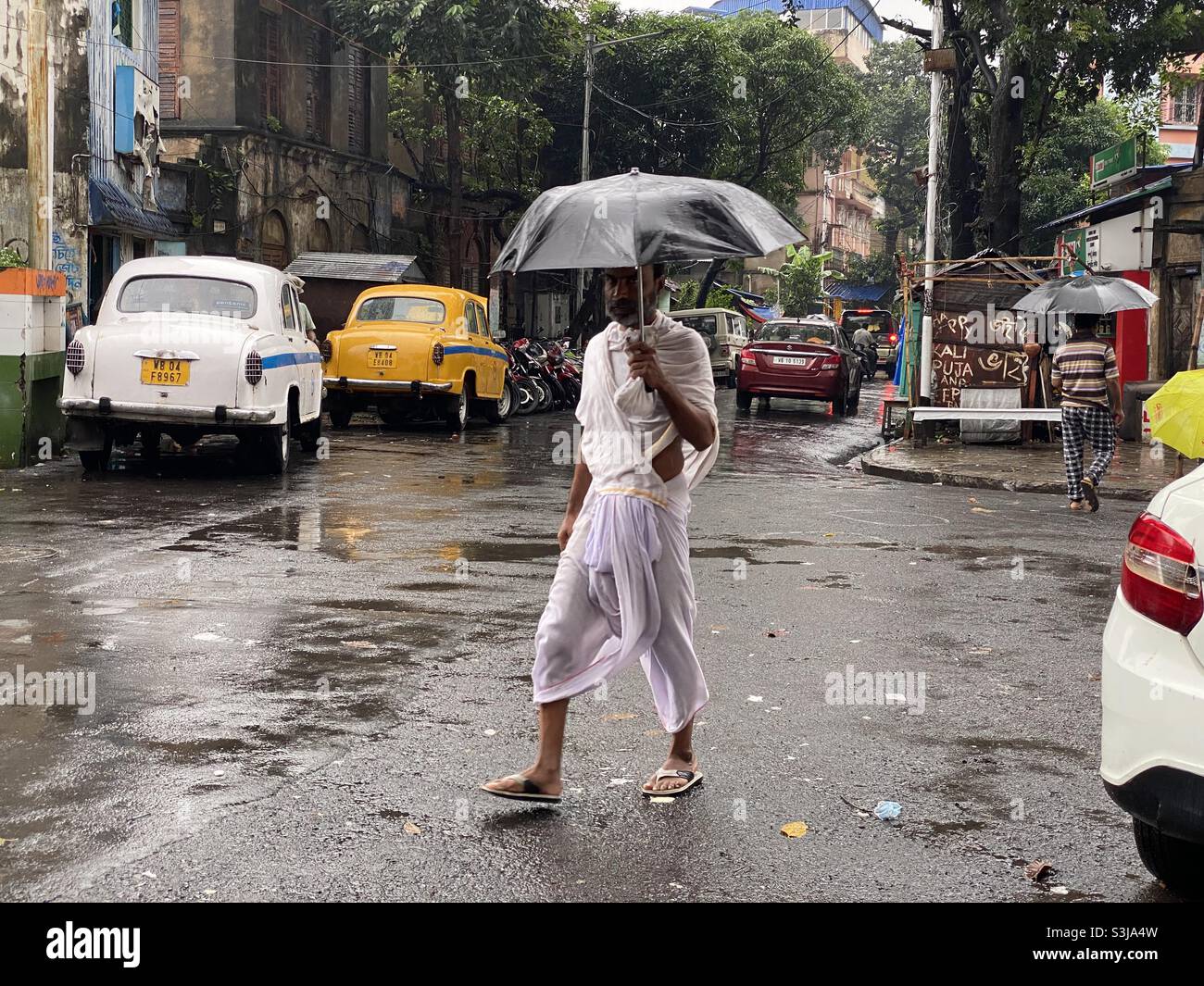 A man wearing traditional Indian dress and walking through road in a rainy day - Smartphone Captured Stock Image