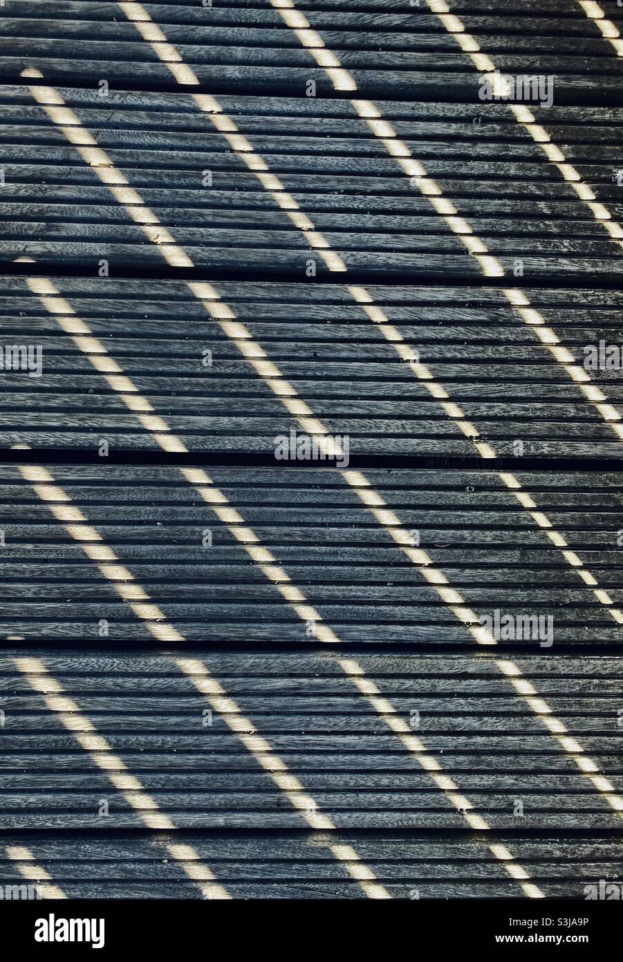 The sunshine makes a striped pattern fall on the wooden planks of a terrace - Smartphone Captured Stock Image