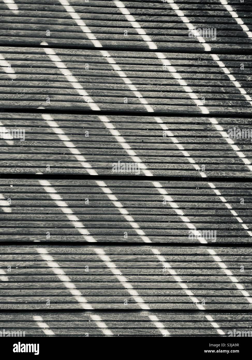The sunshine makes a striped pattern fall on the wooden planks of a terrace - Smartphone Captured Stock Image