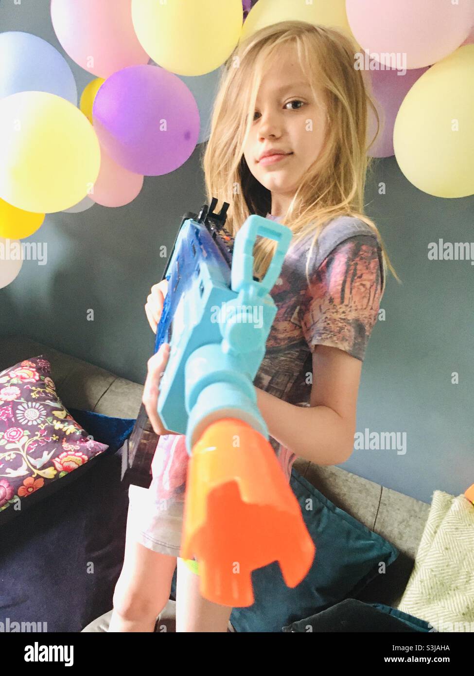 A young boy during his birthday party with a nerf gun and colourful balloons. Stock Photo